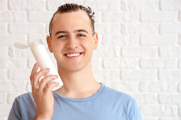 Young man with bottle of shampoo on white brick background