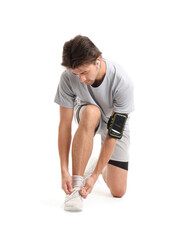 Young man in sportswear tying shoelaces on white background