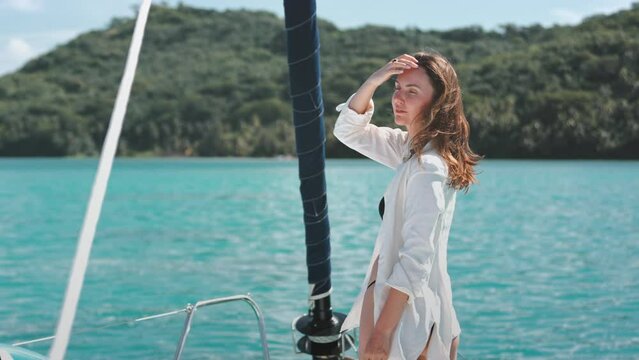 Woman in white shirt relaxes standing on yacht deck. Caucasian girl enjoys beautiful sea green island landscape. Travel, tourism, holiday yacht tour to Bora Bora islands. Slow motion 4K