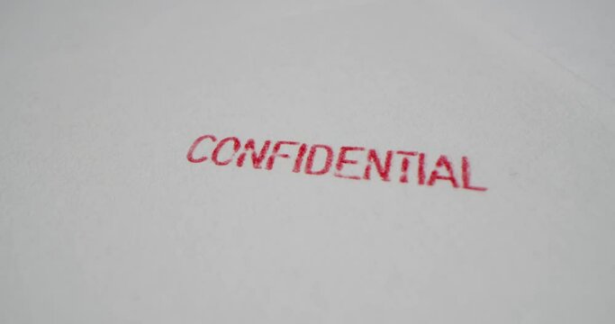 A stamp CONFIDENTIAL is placed on a sheet of white paper, close-up
