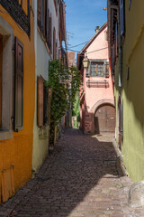 Obraz premium Riquewihr, France - 09 04 2023: The wine route. View of a typical colorful street in downtown with vineyards in background.