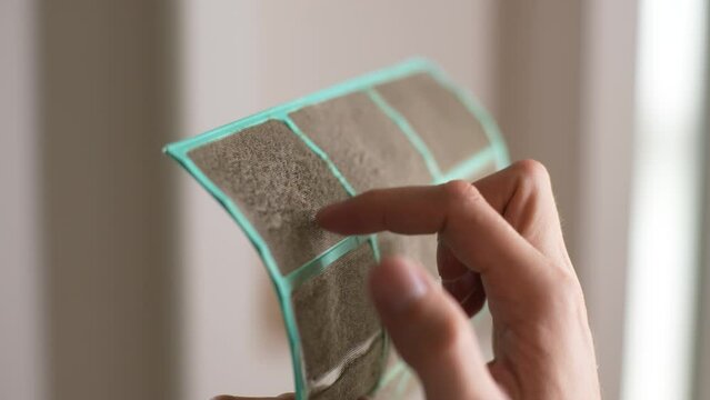 Closeup of unrecognizable man running finger over air conditioner filter membrane before cleaning. Concept for maintenance of hygiene and pure air to prevent allergies. Shooting in slow motion.