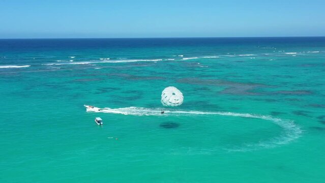 People having fun doing paraseiling in Atlantic ocean with reef and turquoise water, caribbean vacation. Aerial view