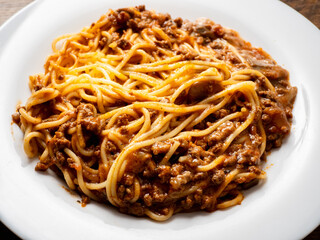 Portion of high quality spaghetti Bolognese on white plate and wooden table. Premium quality dish made with fine products.