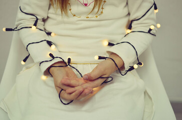 Christmas lights in the hands of a girl in a white dress.