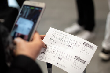 Close-up of a woman using her cell phone to photograph two airline tickets at the airport. Air Transport. Travel concept. - obrazy, fototapety, plakaty