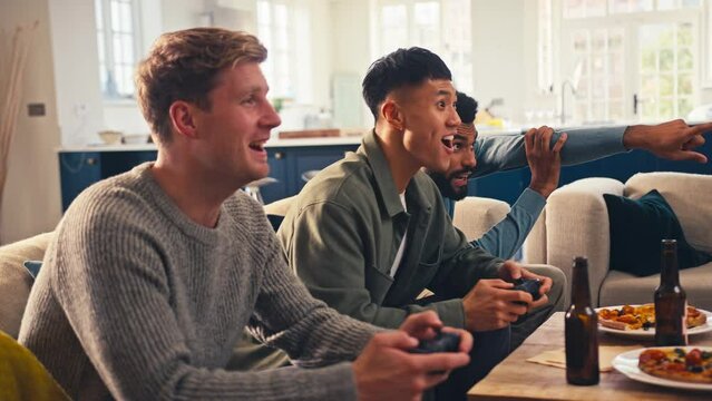 Group of excited male friends gaming at home in lounge with pizza together - shot in slow motion