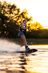 Female wakeboarder wakesurfing on sunset. Girl riding waterski cabel. Holding tow rope. Summer...