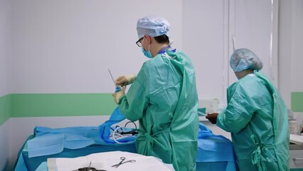 Doctor puts on protective sleeve on the surgical device. Female nurse comes up to arrange medical instruments. - Powered by Adobe