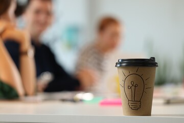 Team of employees working together in office. Paper cup of drink on white table, selective focus