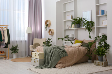Stylish bedroom with comfortable bed and different houseplants. Interior design