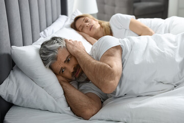 Irritated man covering his ears in bed at home Problem with snoring wife