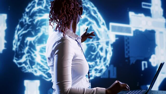 African american woman writing artificial intelligence script code in startup workspace on laptop terminal. Hardworking employee doing maintenance work in high tech facility updating AI systems