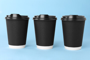 Paper cups with black lids on light blue background. Coffee to go