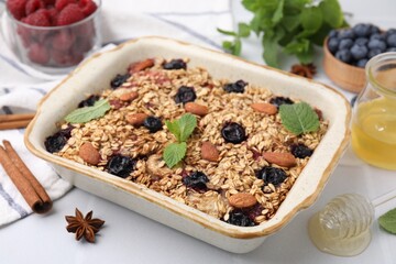 Tasty baked oatmeal with berries, almonds and spices in baking tray on white table, closeup