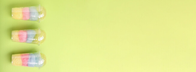 Obraz premium Colorful cotton candies in plastic cups on light green background, top view. Banner design with space for text