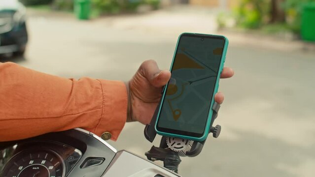 Close-up shot of hand of anonymous black man holding smartphone with digital city map app, requesting route to destination, then putting gadget into holder on scooter and fixing itClose-up shot of han
