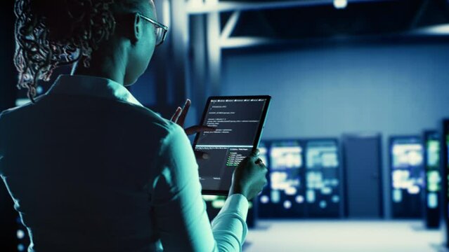 Knowledgeable woman running code on tablet, troubleshooting and upgrading high tech establishment equipment designed to accommodate supercomputers, networking systems and storage arrays