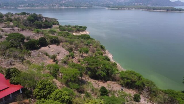 Aerial flyover: Rugged hilly lake shore in tropical El Salvador mtns