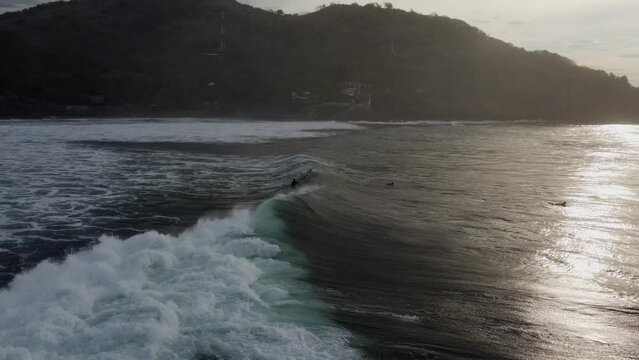Surfer rides big, pushy shore break surf wave in golden dusk lighting