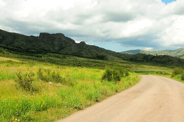 Fototapeta na wymiar A gravel road turns through a valley at a high cliff under a cloudy summer sky.