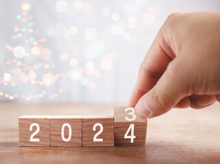 Wooden blocks Happy New Year 2024. Hand holding wooden blocks on white background and bokeh. Action...