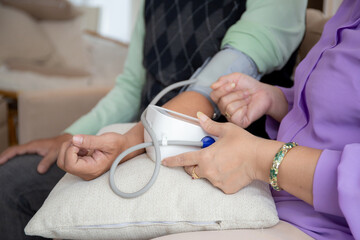Closeup hands asian senior couple sitting on sofa checking blood pressure with pressure gauge in living room at home, elderly man and woman checkup health and pressure, medical of patient.