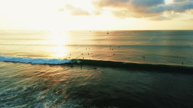 Aerial view of surfers catching a wave in the ocean during sunset. In golden hour, the sky is orange and reflected from the water. Surfers catch big waves in the ocean, an extreme sport.