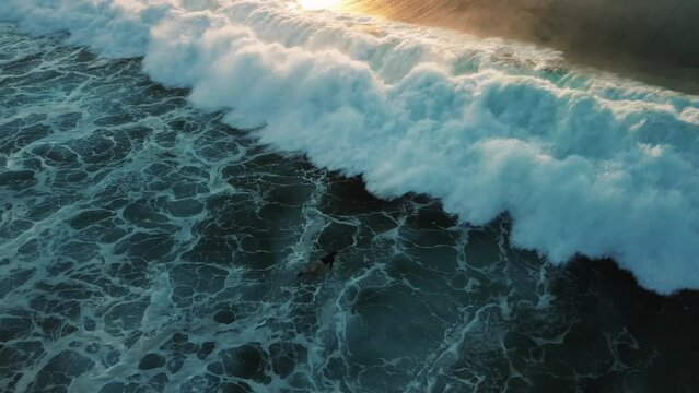 Aerial view of a surfer lying down on a surfboard towards the line-up. Surfer struggling with a strong wave in the foam. Diving under a wave, paddling on a surfboard, extreme sport.