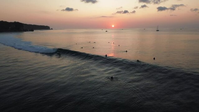 Bird's eye view of a surfer conquering a wave and rolling in a tube. Surfing during sunset, in the evening. Scenic drive of a surfer in the wave. Unidentifiable silhouette of a surfer during sunset.