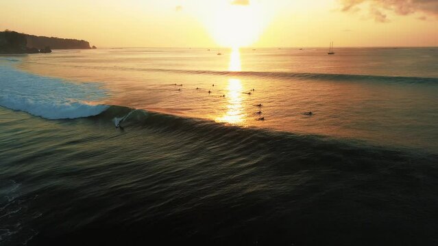 Top-down view of the ocean during sunset, with surfers catching big waves. A group of surfers is waiting for big waves on the line-up, waiting for a swell. Surfing during sunset, golden hour.