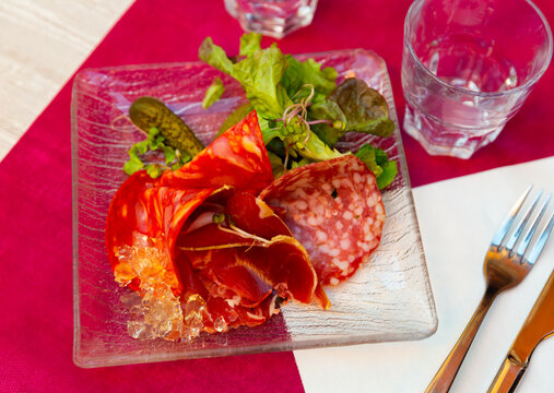 Appetizing assorted meat of smoked sausage and sliced carbonad, served with pickled cucumbers and lettuce