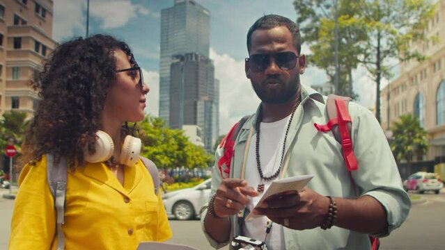 Medium shot of African American man and Caucasian girlfriend standing together in Saigon city centre while on sightseeing trip, pointing, reading information in booklet and looking around