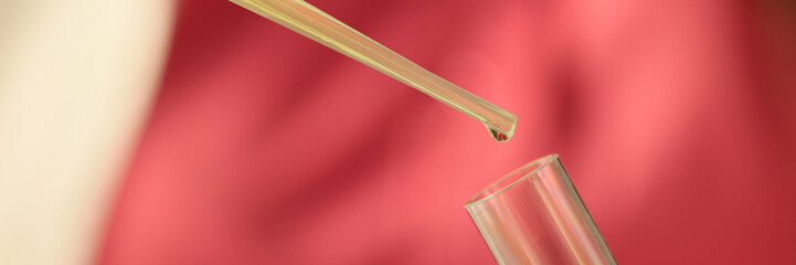 Liquid from pipette drips into test tube close-up.