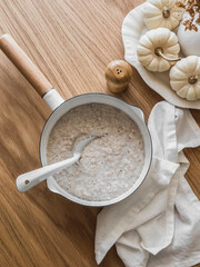 Simple oatmeal porridge in a saucepan on a wooden table, top view. Delicious healthy breakfast