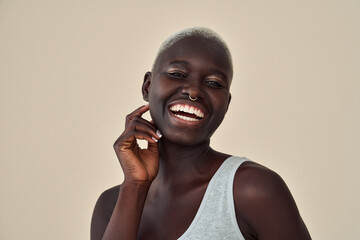 Happy young Black woman beauty female model, cool gen z African lady with short blond hair healthy face skin, nose piercing and wide smile looking at camera isolated at beige background. Portrait.