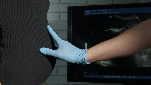 Hand in gloves by pregnant belly. A view of hand in rubber glove try to examine the pregnant woman against ultrasound picture in the cabinet.