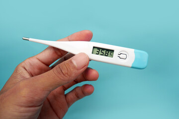 A man's hand holding a digital thermometer in her hand on a blue background. A person looks at an electronic thermometer with temperature.