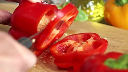 Close-up of male hands cutting red pepper on a wooden board. Slicing fresh vegetables with a knife.


