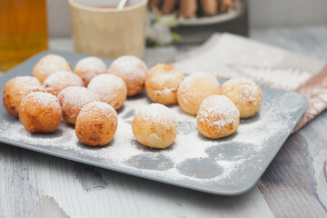 Curd donuts in powdered sugar on a plate, round donuts with a cup of tea