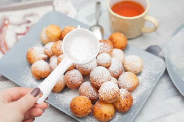 Curd donuts in powdered sugar on a plate, round donuts with a cup of tea