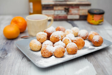 Curd donuts in powdered sugar on a plate, round donuts with a cup of tea