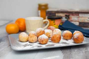 Curd donuts in powdered sugar on a plate, round donuts with a cup of tea