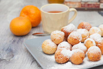 Curd donuts in powdered sugar on a plate, round donuts with a cup of tea