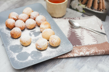 Curd donuts in powdered sugar on a plate, round donuts with a cup of tea