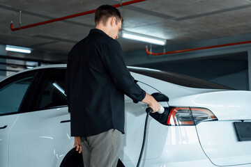 Young man travel with EV electric car to shopping center parking lot charging in downtown city...