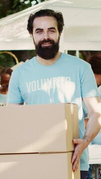 Vertical video Generous man volunteering at neighborhood food drive, distributing non-perishable rations to the hungry and homeless. While holding donation box, caucasian charity worker looks at