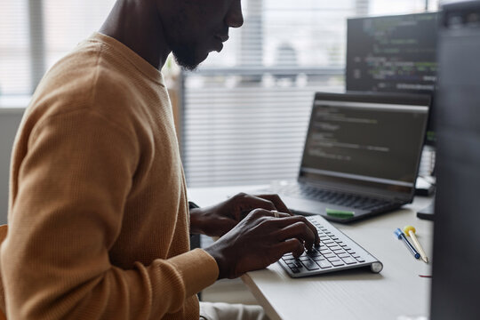 African American programmer writing codes for program while sitting at table in IT office