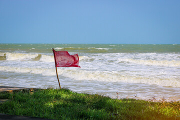 Red warning flag flapping in the wind on beach at stormy weather. Swimming is dangerous in sea...
