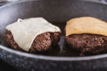 Juicy ground beef hamburger patty in a frying pan, crowned with melting cheese